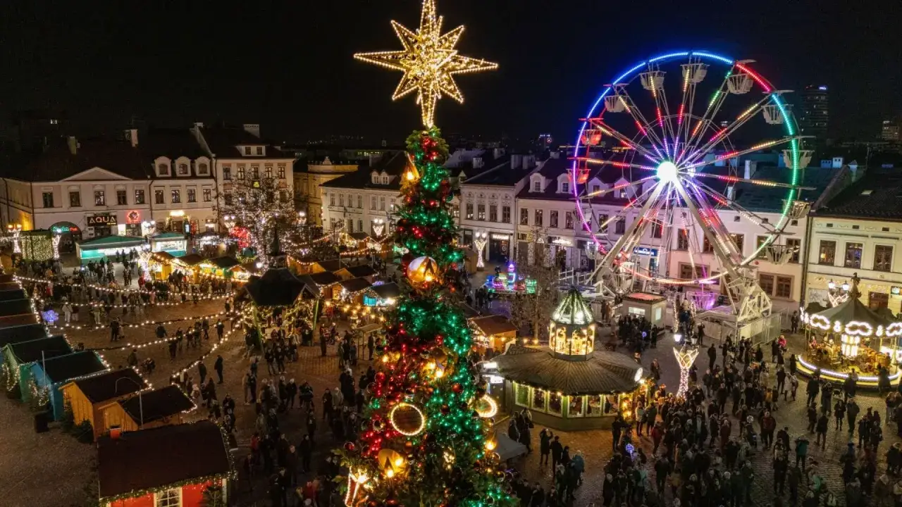 Tłum ludzi spaceruje po jednym z najpiękniejszych jarmarków bożonarodzeniowych, podziwiając iluminacje, choinkę i diabelski młyn.