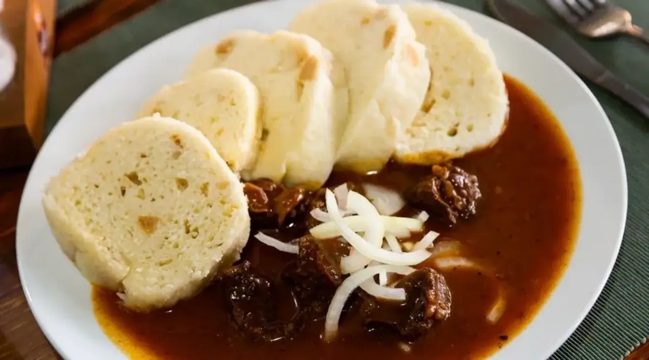 Gulasz z wołowiny z knedlami, klasyczne dania kuchni czeskiej. Aromatyczny sos i miękkie kluski tworzą sycącą potrawę.
