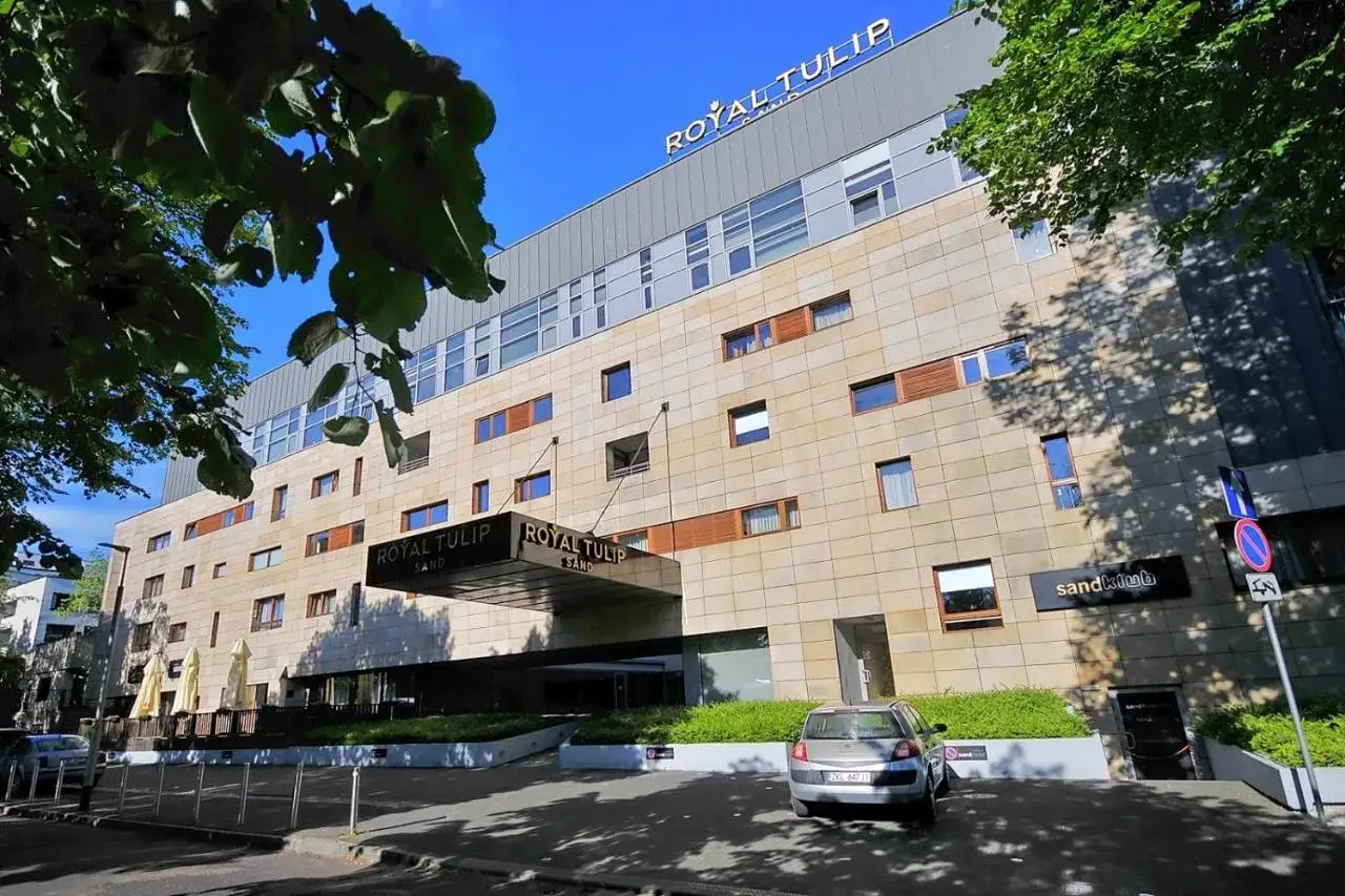 Nowoczesny hotel Royal Tulip Sand w Kołobrzegu, z kamienną fasadą i dużymi oknami, zaprasza na wypoczynek.