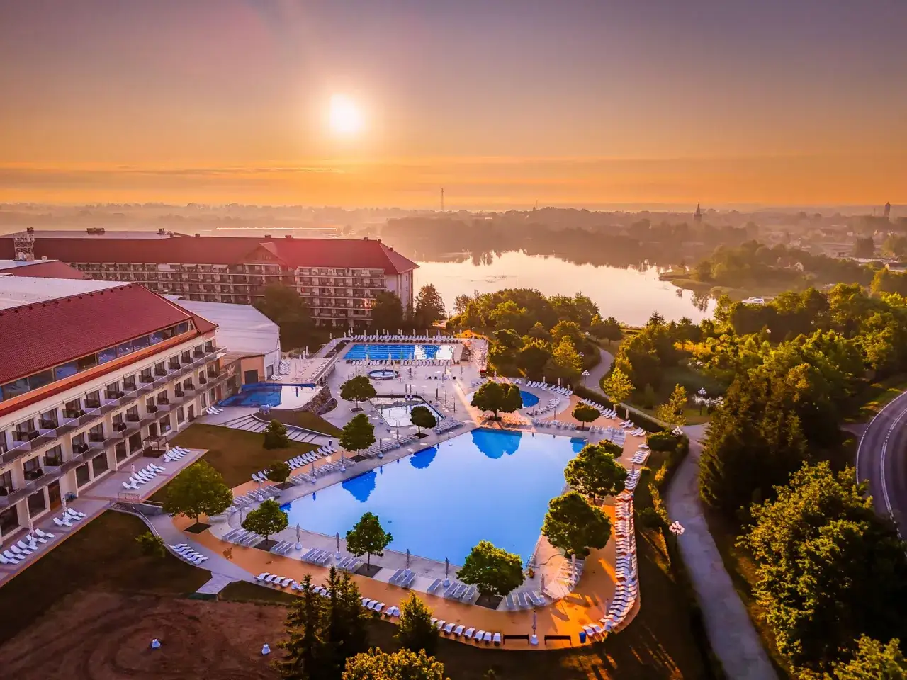 Hotel Gołębiewski Mikołajki, z basenami i jeziorem w tle, o wschodzie słońca. Rok budowy nieznany.