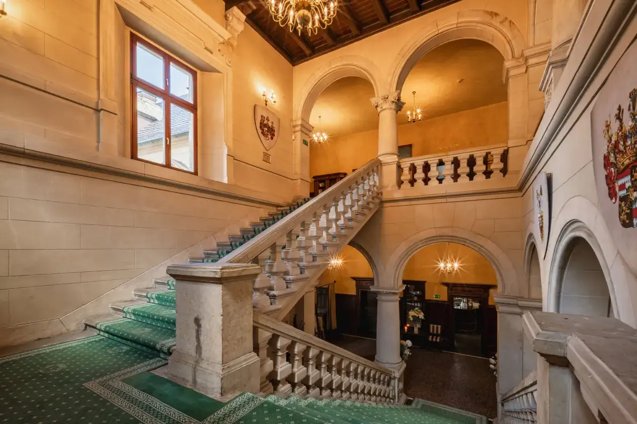 Elegancka klatka schodowa w zamku Kliczków, z zielonym dywanem i kamiennymi balustradami. Sprawdź zamek Kliczków ceny pobytu.