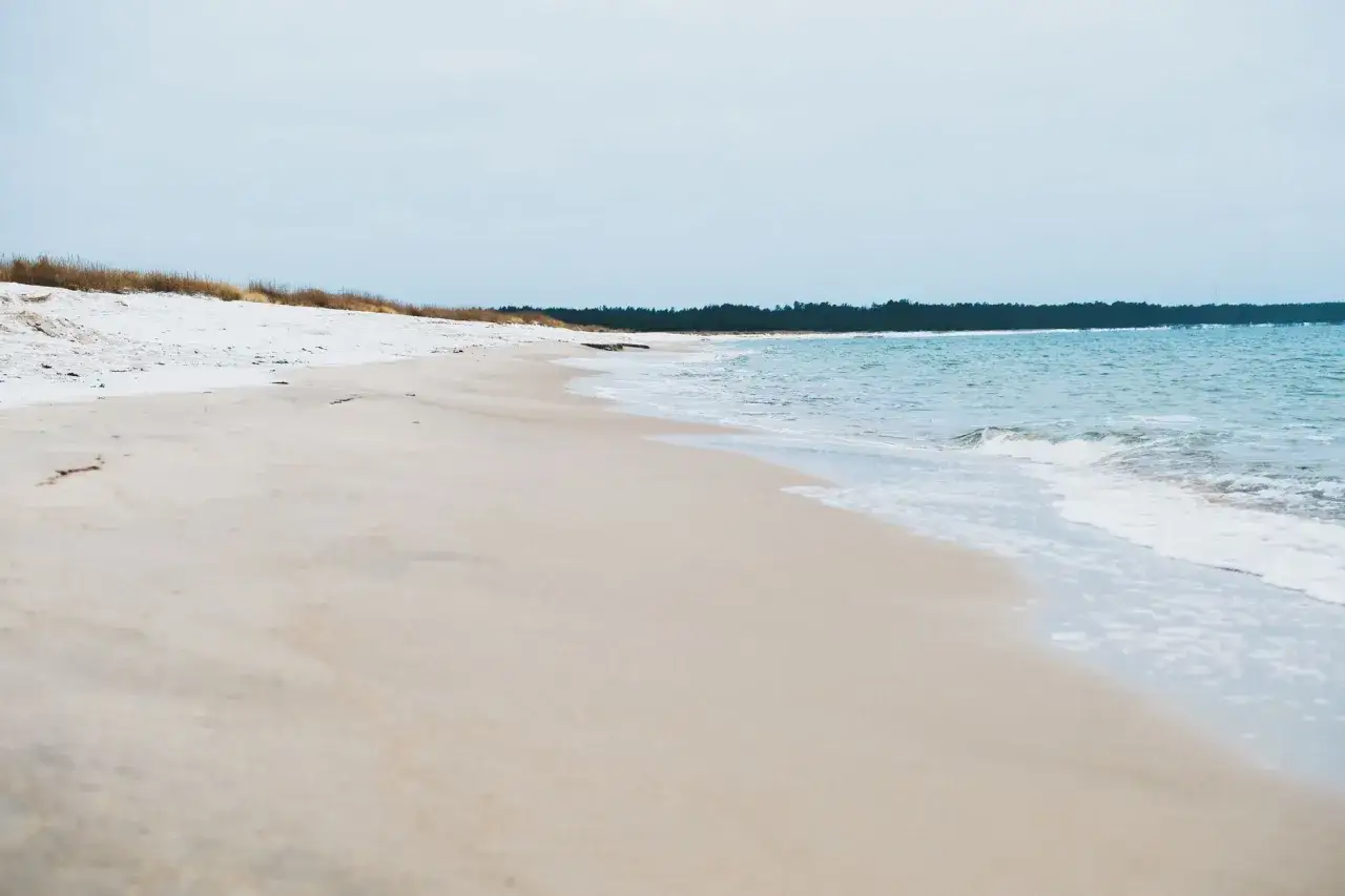 Piaszczyste, białe plaże w Polsce, gdzie morze delikatnie muska brzeg.