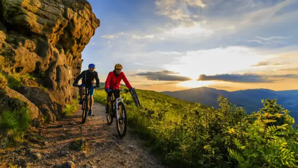 Dwóch rowerzystów przemierza malowniczą ścieżkę, odkrywając jedne z najpiękniejszych tras rowerowych w Polsce. Zachód słońca maluje niebo nad górami.