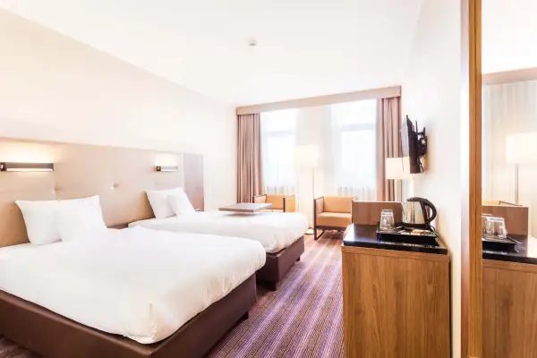 Pokój dwuosobowy w hotelu DeSilva Poznań z dwoma wygodnymi łóżkami, stolikiem i miejscem do przygotowania kawy.