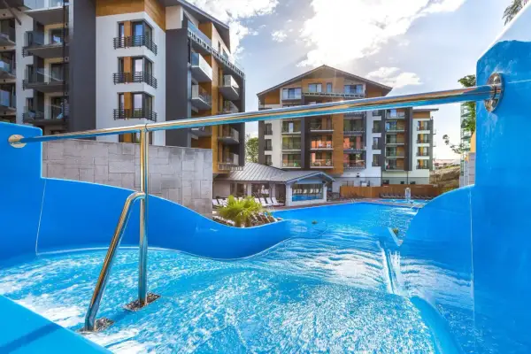 Basen z falą i zjeżdżalnią w hotelu Blue Mountain w Szklarskiej Porębie. Nowoczesne budynki hotelowe w tle.