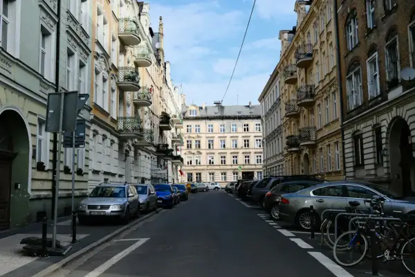 Ulica w kamienicach, typowa dla **południa Polski**. Samochody stoją zaparkowane wzdłuż chodnika, a na pierwszym planie widać rowery.