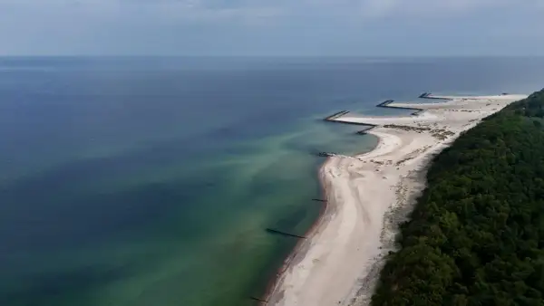 Widok z lotu ptaka na plażę w Jarosławcu z kamiennymi falochronami tworzącymi kształt przypominający molo.