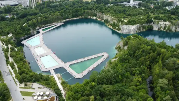 Wakacyjny wypoczynek nad wodą w Krakowie. Drewniane pomosty z basenami i leżakami otaczają turkusowe jezioro w otoczeniu zieleni.