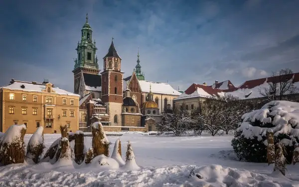 Zamek Królewski na Wawelu w zimowej scenerii. Pokryte śniegiem dachy i drzewa tworzą magiczny widok, idealny na kraków atrakcje zimą.