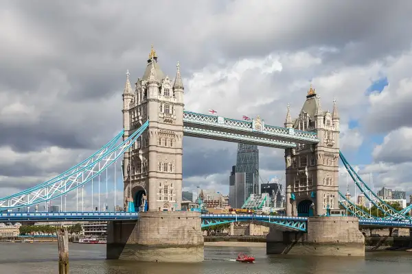 Słynny most w Wielkiej Brytanii, Tower Bridge, z charakterystycznymi wieżami i niebieskimi linami, na tle pochmurnego nieba.