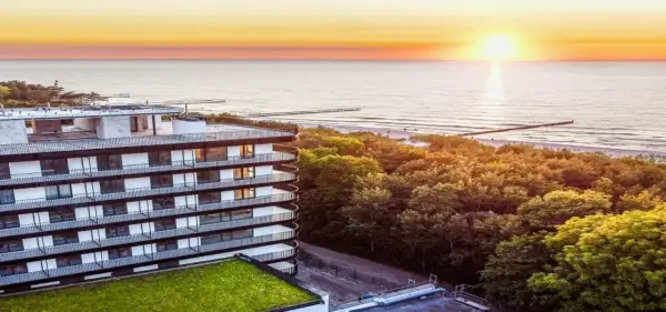 Idealny urlop nad morzem z wyżywieniem: nowoczesny hotel z widokiem na zachód słońca nad Bałtykiem, otoczony zielenią.