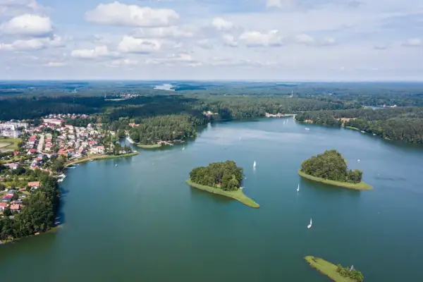 Malownicze jeziora w Polsce, z wyspami porośniętymi drzewami i żaglówkami na wodzie, otoczone lasami i domami.
