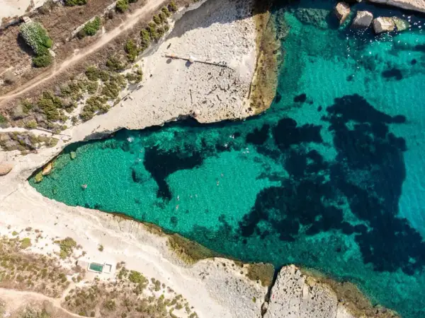 Malta plaże: turkusowa woda zatoki, skaliste wybrzeże i kilka osób kąpiących się w słońcu.