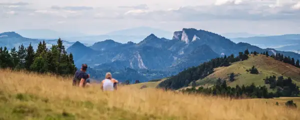 Para odpoczywa na trawiastym zboczu, podziwiając malownicze góry w okolicy Szczawnicy.