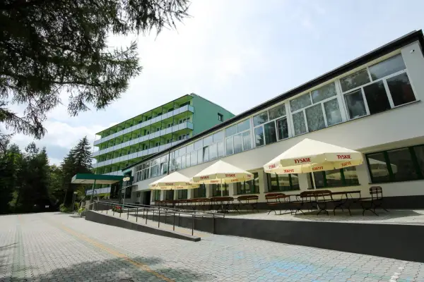 Zielony budynek sanatorium z balkonami i tarasem z parasolami Tyskie. Miejsce idealne dla szukających najlepszych sanatoriów w Polsce.