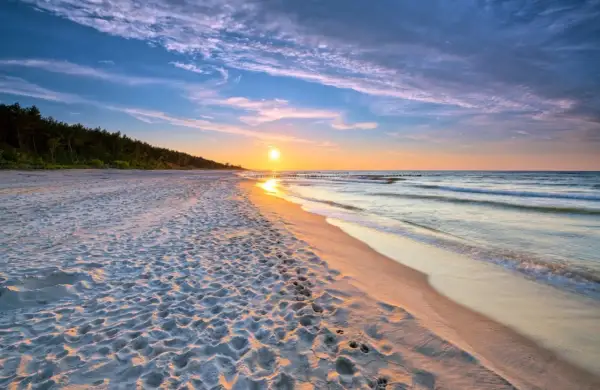 Zachód słońca nad morzem, piaszczysta plaża z odciskami stóp, las w tle. Idealne, fajne miejsce nad morzem dla dwojga na romantyczny spacer.