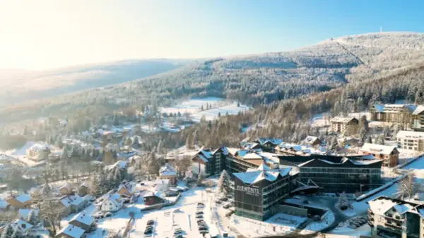 Zimowy krajobraz z hotelem Elements, który oferuje idealny hotel ze stokiem. Wokół ośnieżone drzewa i góry.