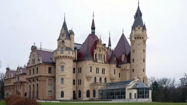 Kamienny zamek z czerwonymi dachami i wieżami, przypominający najstarsze zamki w Polsce.